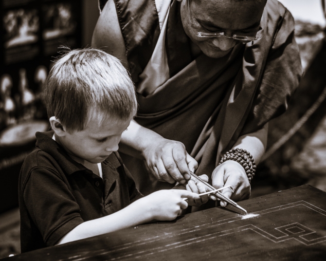 A monk demonstrates the process to a young visitor on the community sand painting.